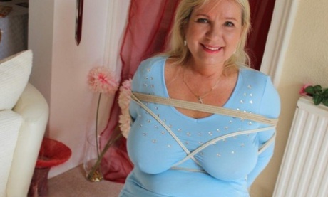 Older blonde is gagged and tied up in a variety of outfits inside her house