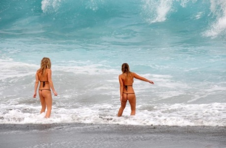 Marry Queen and her lesbian lover remove micro bikinis while the surf comes in