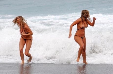 Marry Queen and her lesbian lover remove micro bikinis while the surf comes in