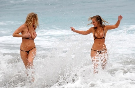 Marry Queen and her lesbian lover remove micro bikinis while the surf comes in