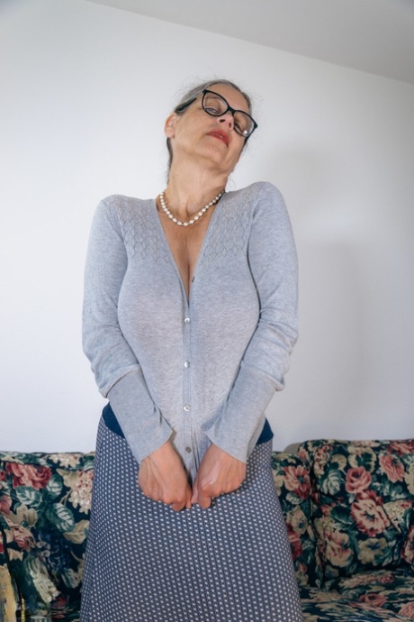 Busty mature woman Busty Tina gets naked on a sofa with her glasses on