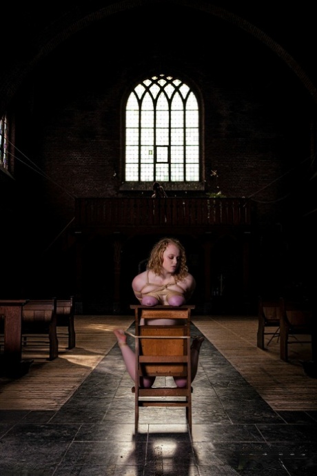 Naked blonde Carmine Worx is left kneeling on a chair while tied up with rope